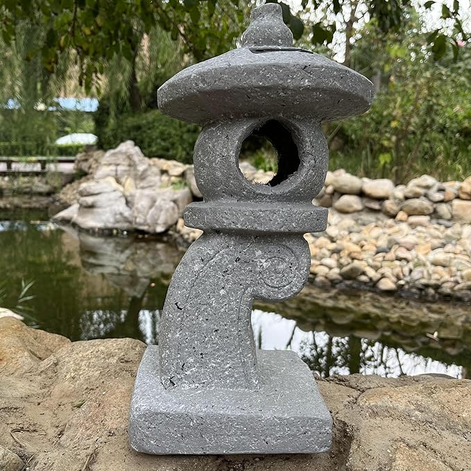 Gray stone lantern on a rock wall with a pond and trees in the background