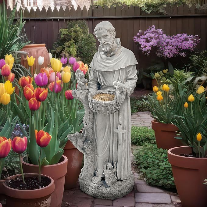 Statue of a monk holding a basket in a garden with colorful tulips and potted plants.