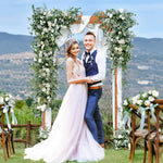 Couple standing under a floral archway with a scenic background