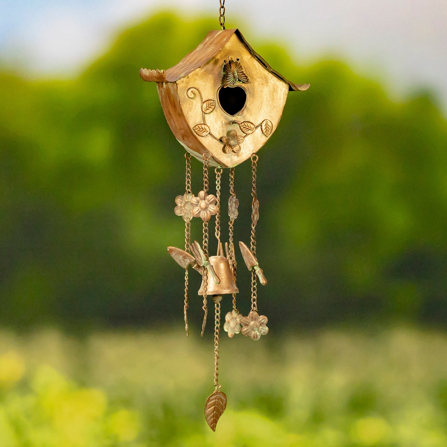 Decorative wind chime shaped like a birdhouse with hanging elements against a blurred green background