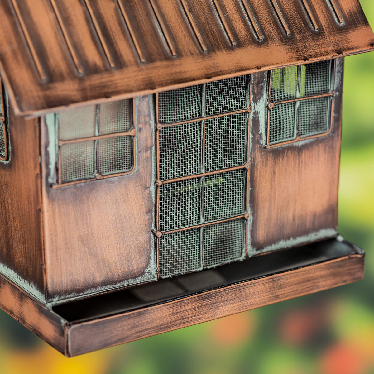 Bronze-colored bird feeder with grid-like design on a blurred natural background