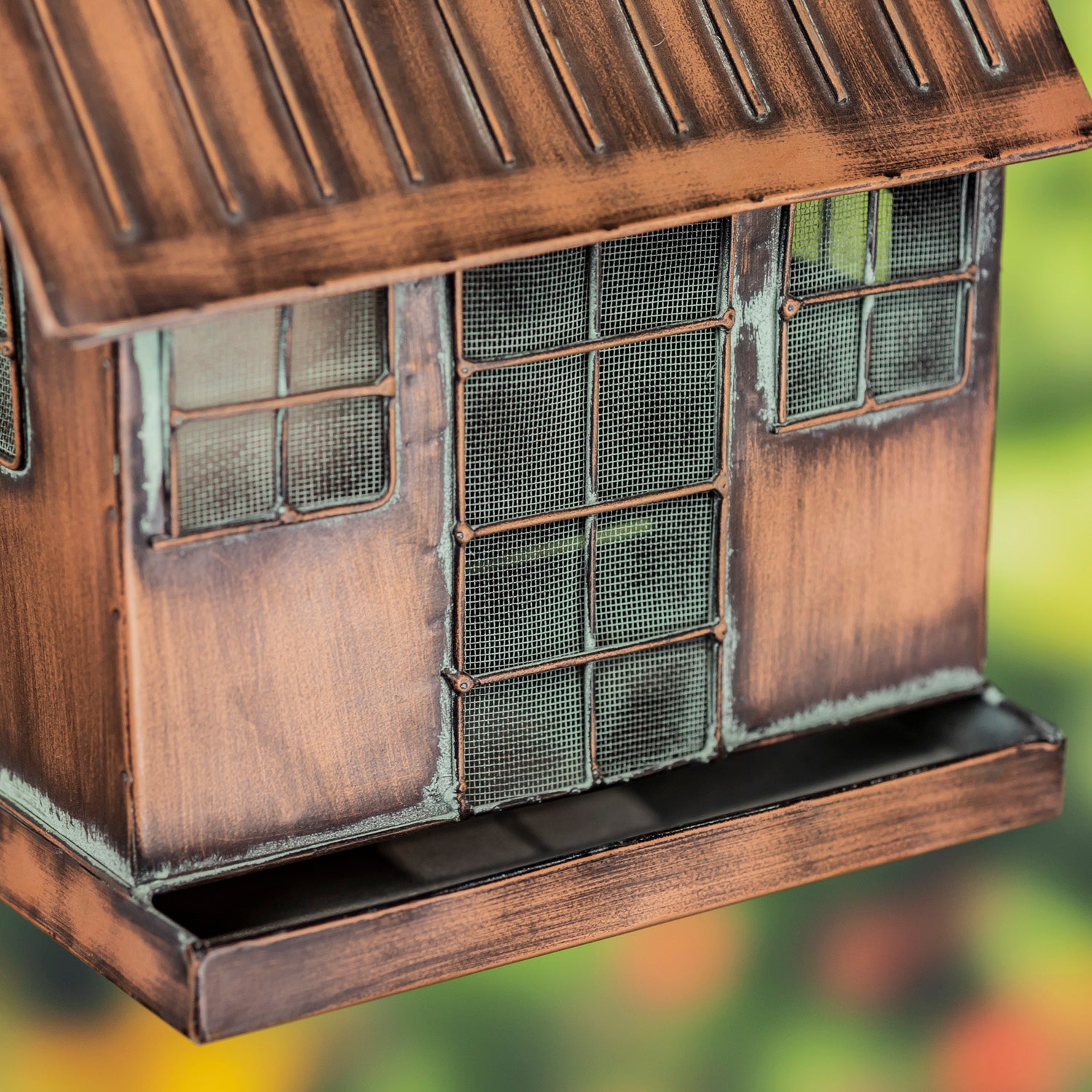 Bronze-colored bird feeder with grid-like design on a blurred natural background
