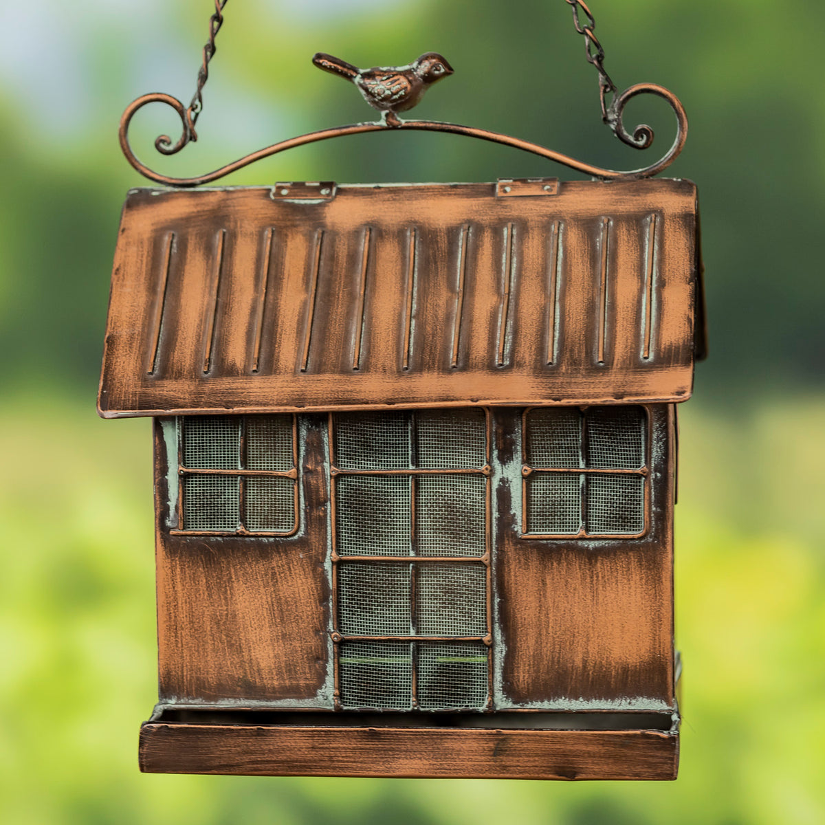 Bronze birdhouse with a bird perched on top against a blurred green background