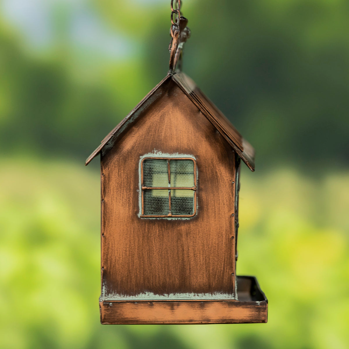 Wooden birdhouse with a window design hanging against a blurred green background