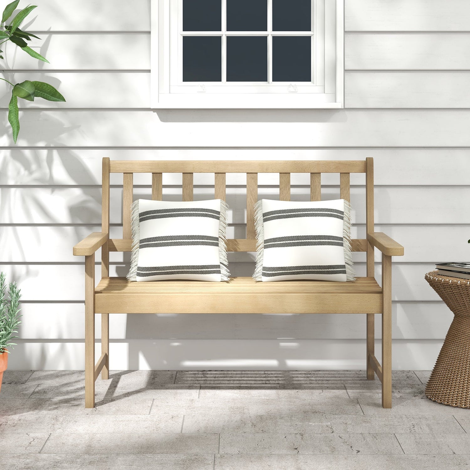 Wooden bench with striped cushions on a patio with a white wall and window in the background.