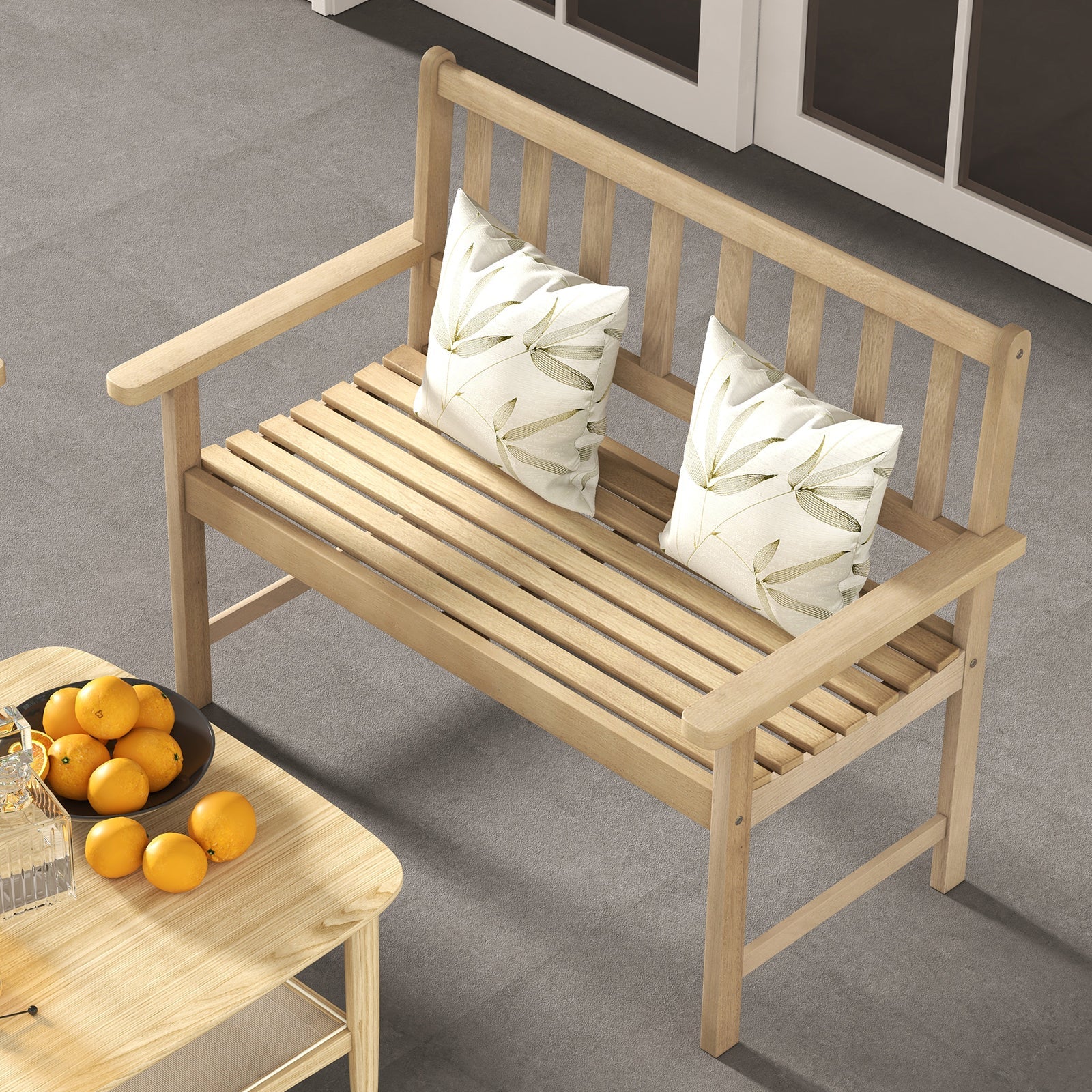 Wooden bench with white pillows on a concrete floor, next to a small table with oranges.
