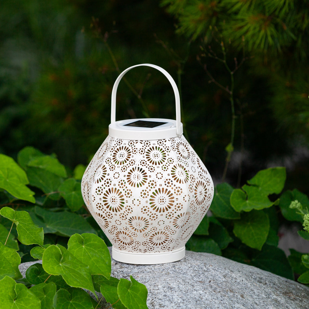 Decorative white lantern with intricate patterns on a rock surrounded by green foliage