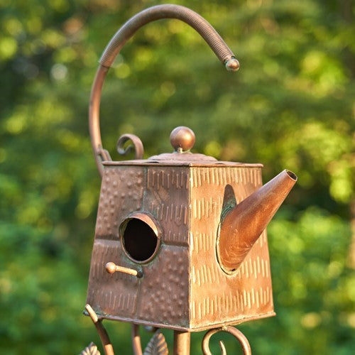 Copper birdhouse shaped like a teapot with a blurred green background