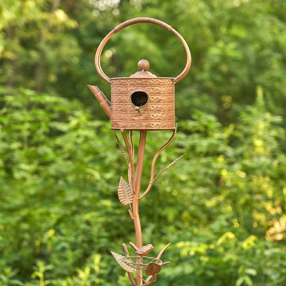 Decorative metal birdhouse shaped like a teapot with a blurred green background