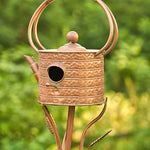 Copper birdhouse with a decorative stand against a blurred green background