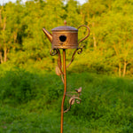 Decorative copper birdhouse shaped like a teapot on a stand with a blurred green background