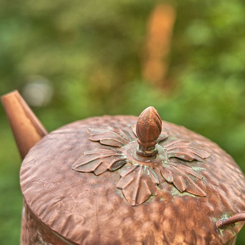 Close-up of a copper teapot with intricate designs against a blurred green background