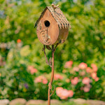 Decorative metal birdhouse on a stick with a blurred garden background