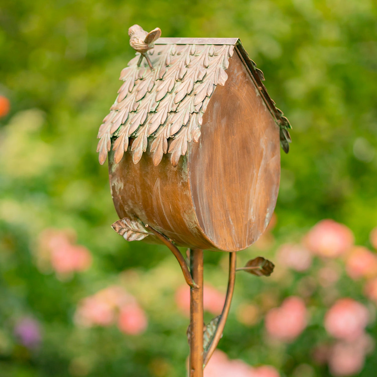 Decorative birdhouse shaped like an acorn with a bird on top, set against a blurred garden background.