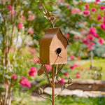 Decorative metal birdhouse on a stand with a garden background