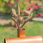 Decorative metal sculpture of a bird and nest on a post with a garden background