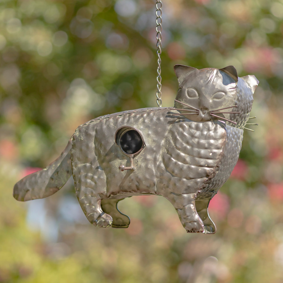 Metallic cat-shaped bird feeder hanging outdoors with a blurred natural background