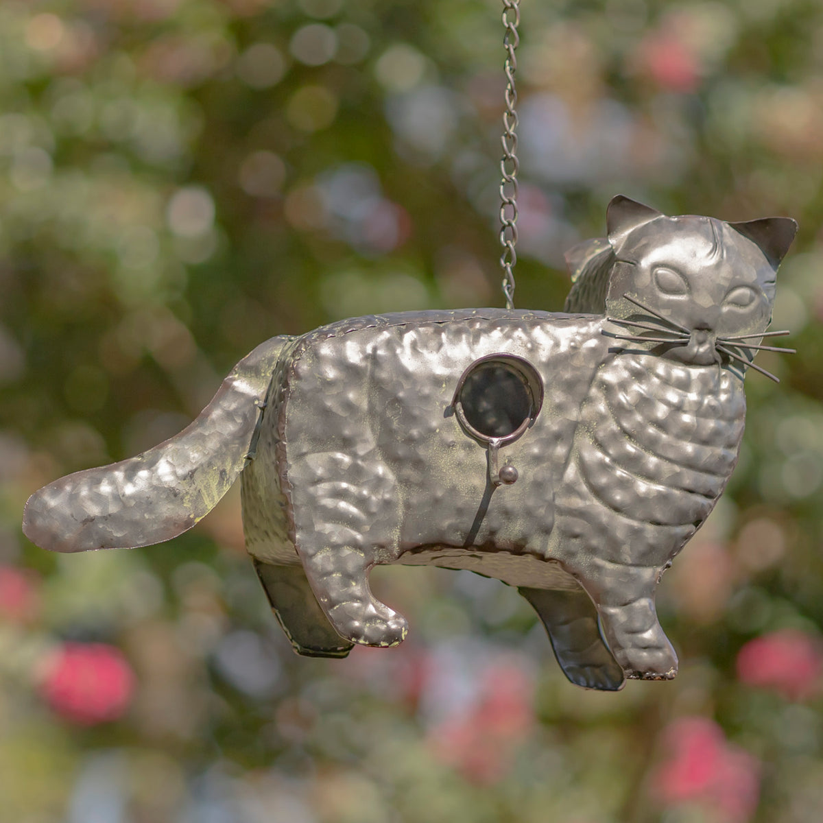 Metallic cat-shaped bird feeder hanging against a blurred natural background