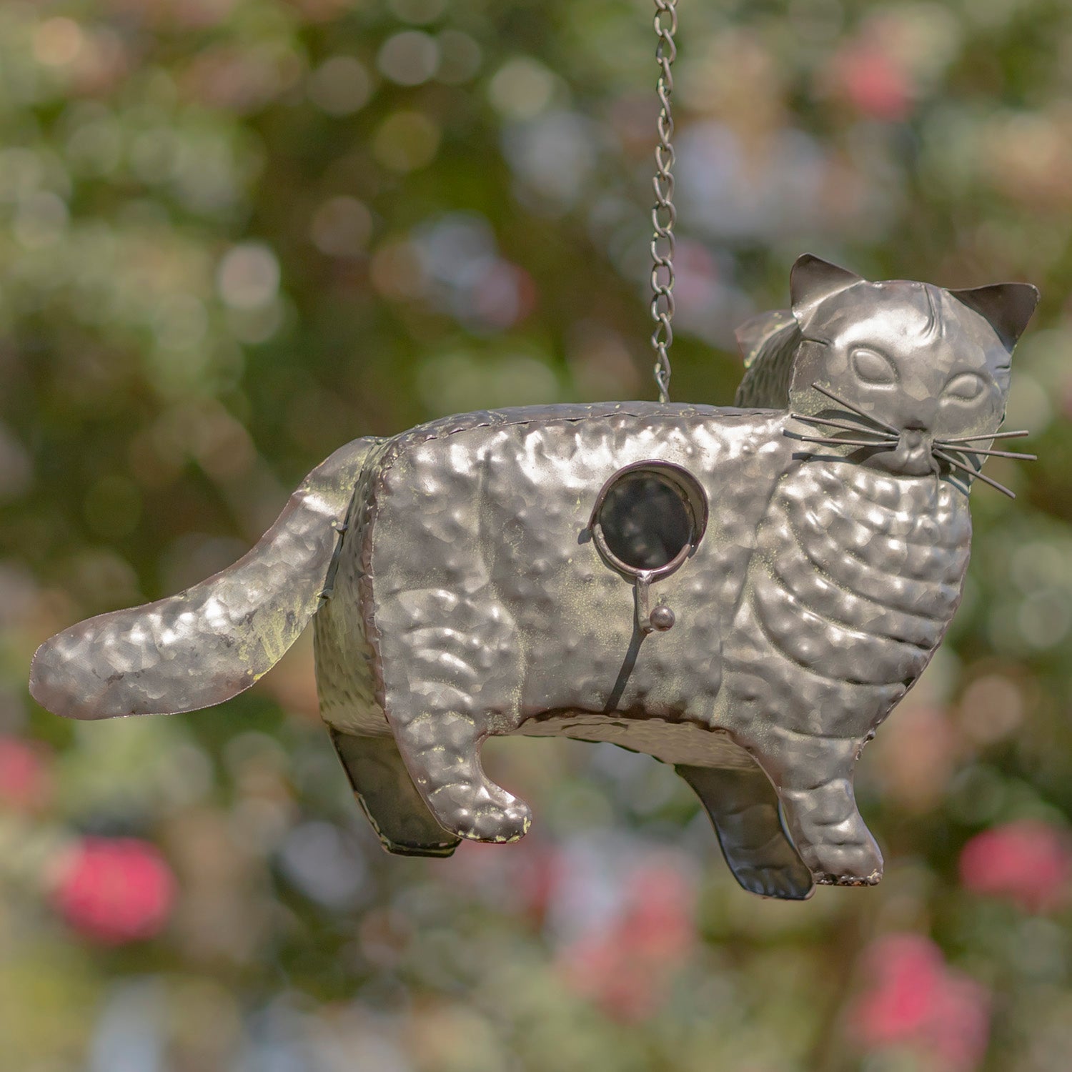 Metallic cat-shaped bird feeder hanging against a blurred natural background