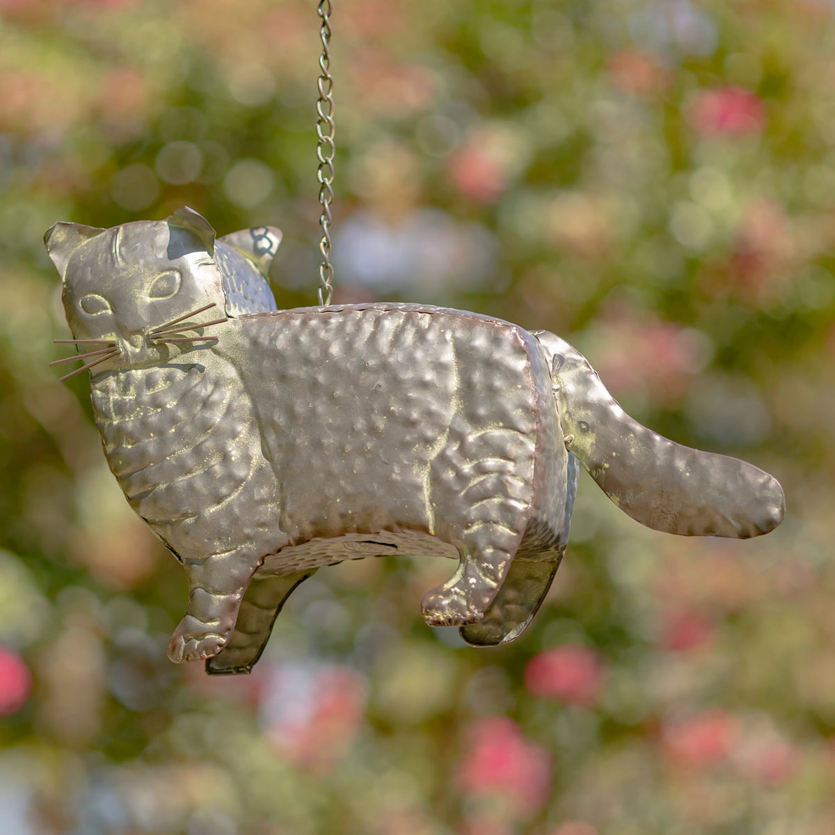 Decorative metal cat-shaped ornament hanging against a blurred natural background