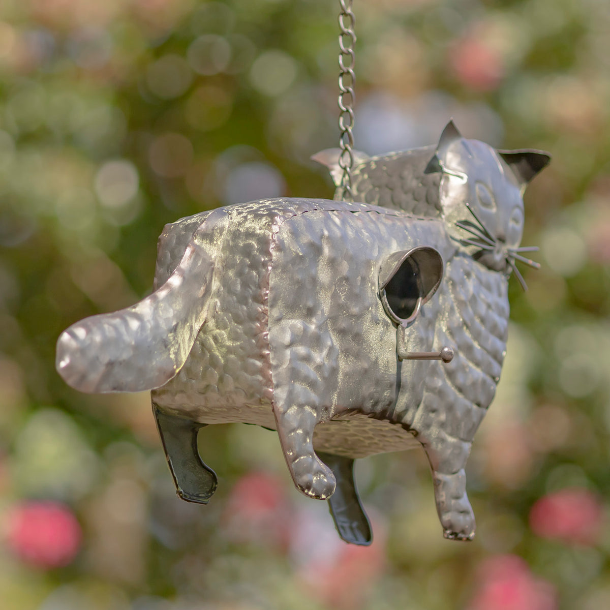 Metallic cat-shaped birdhouse hanging against a blurred natural background
