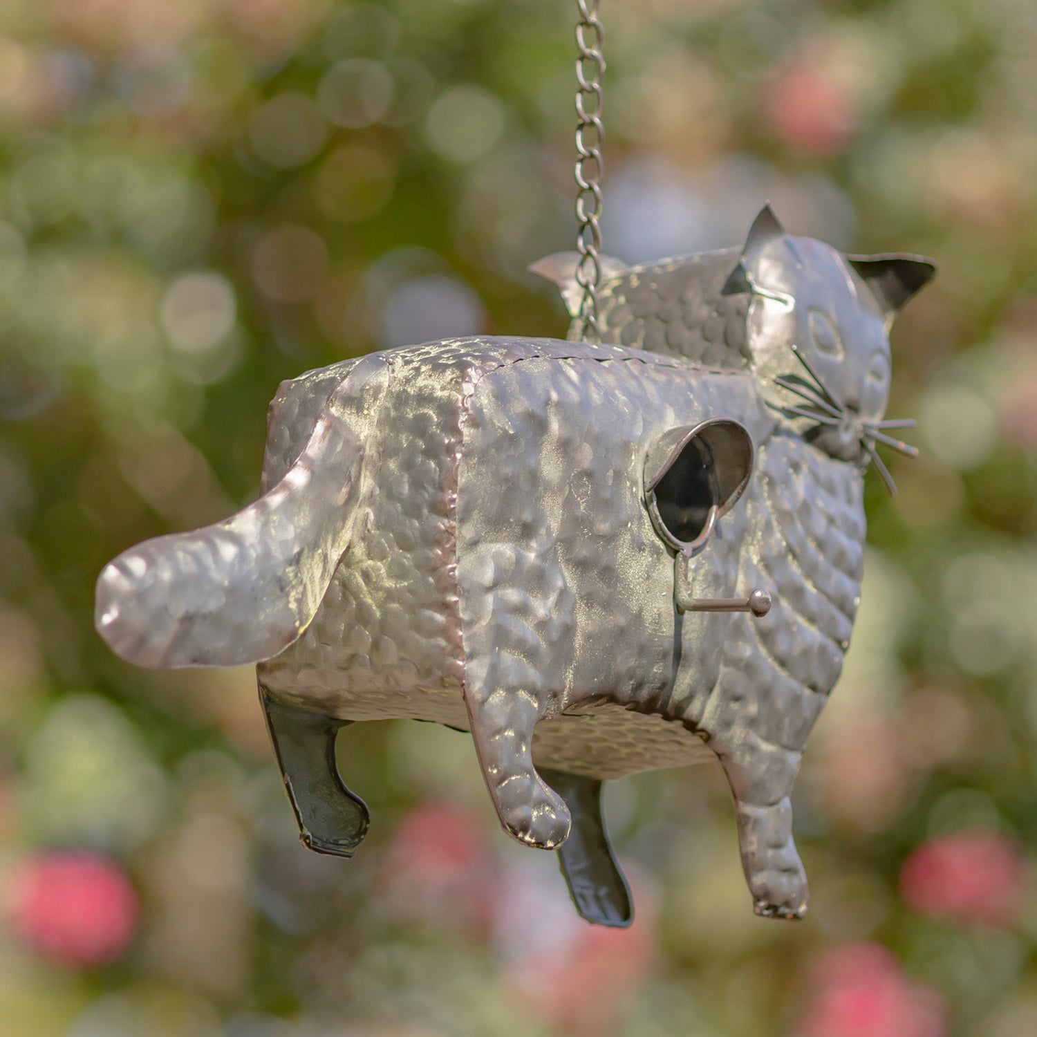 Metallic cat-shaped birdhouse hanging against a blurred natural background