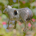 Metallic cow-shaped ornament hanging against a blurred natural background