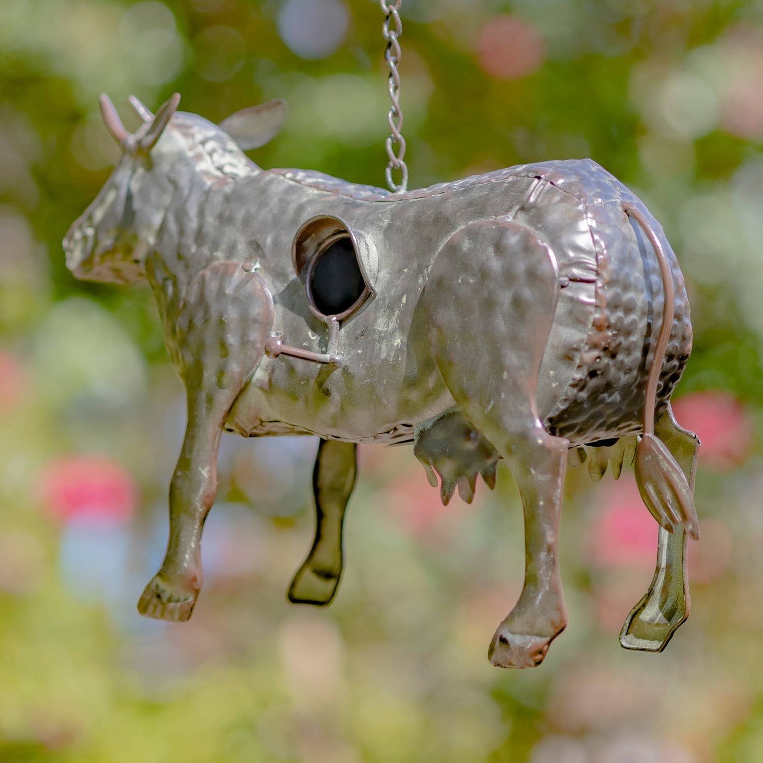 Metallic cow-shaped ornament hanging against a blurred natural background