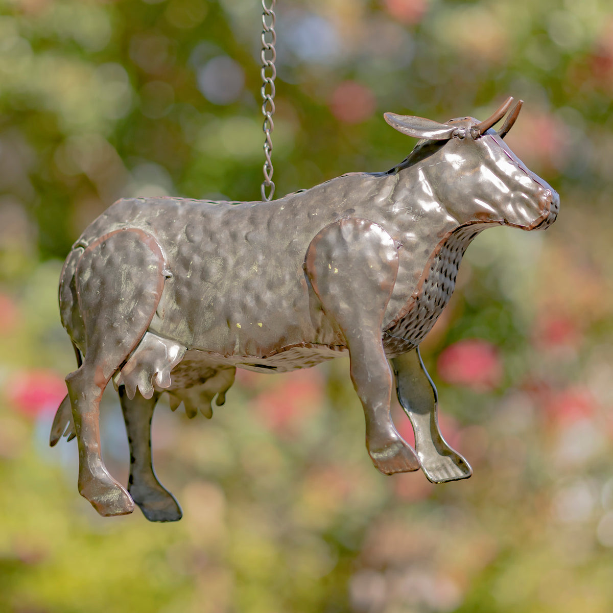Metallic cow-shaped ornament hanging against a blurred natural background