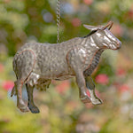 Metallic cow-shaped ornament hanging against a blurred natural background