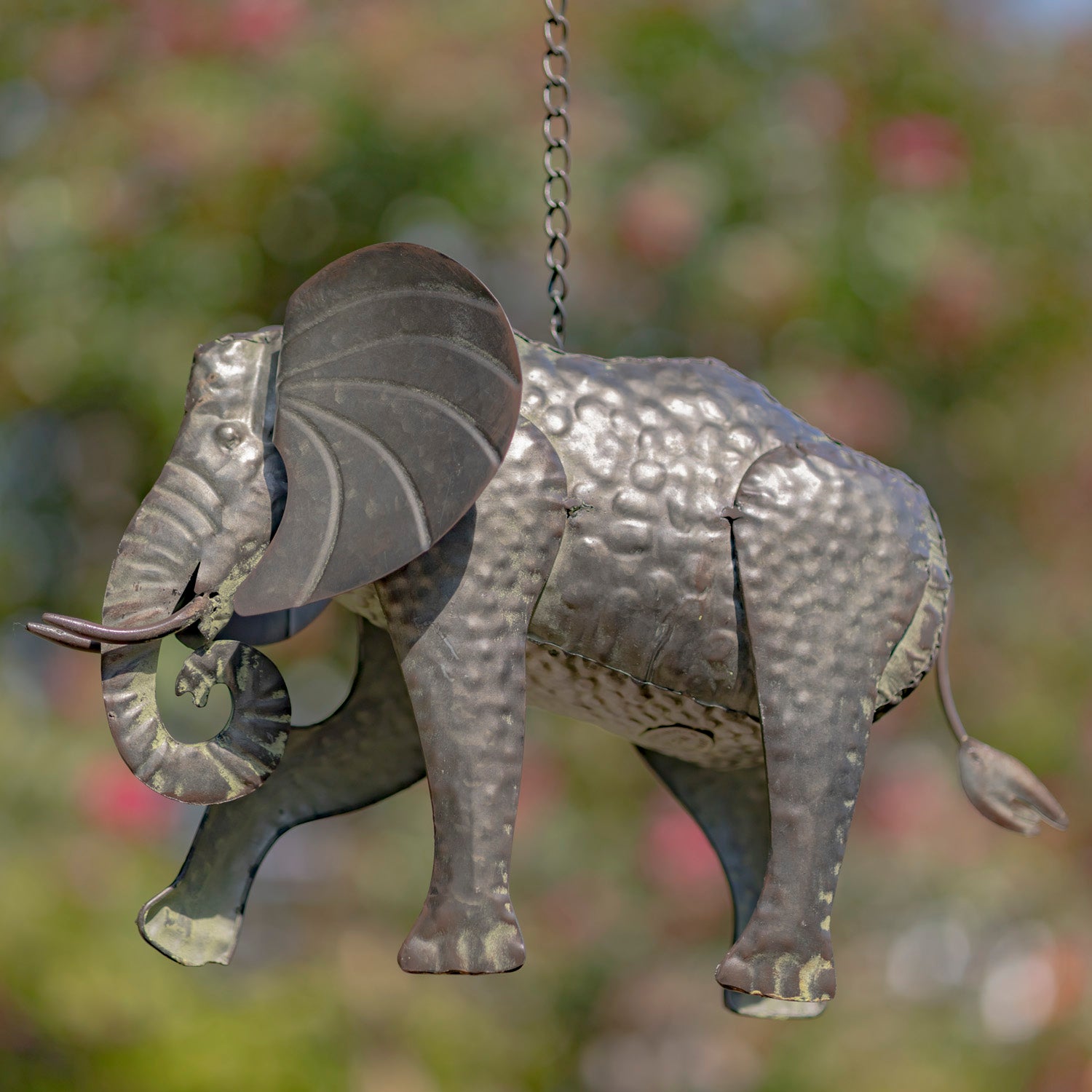 Metallic elephant ornament hanging against a blurred natural background