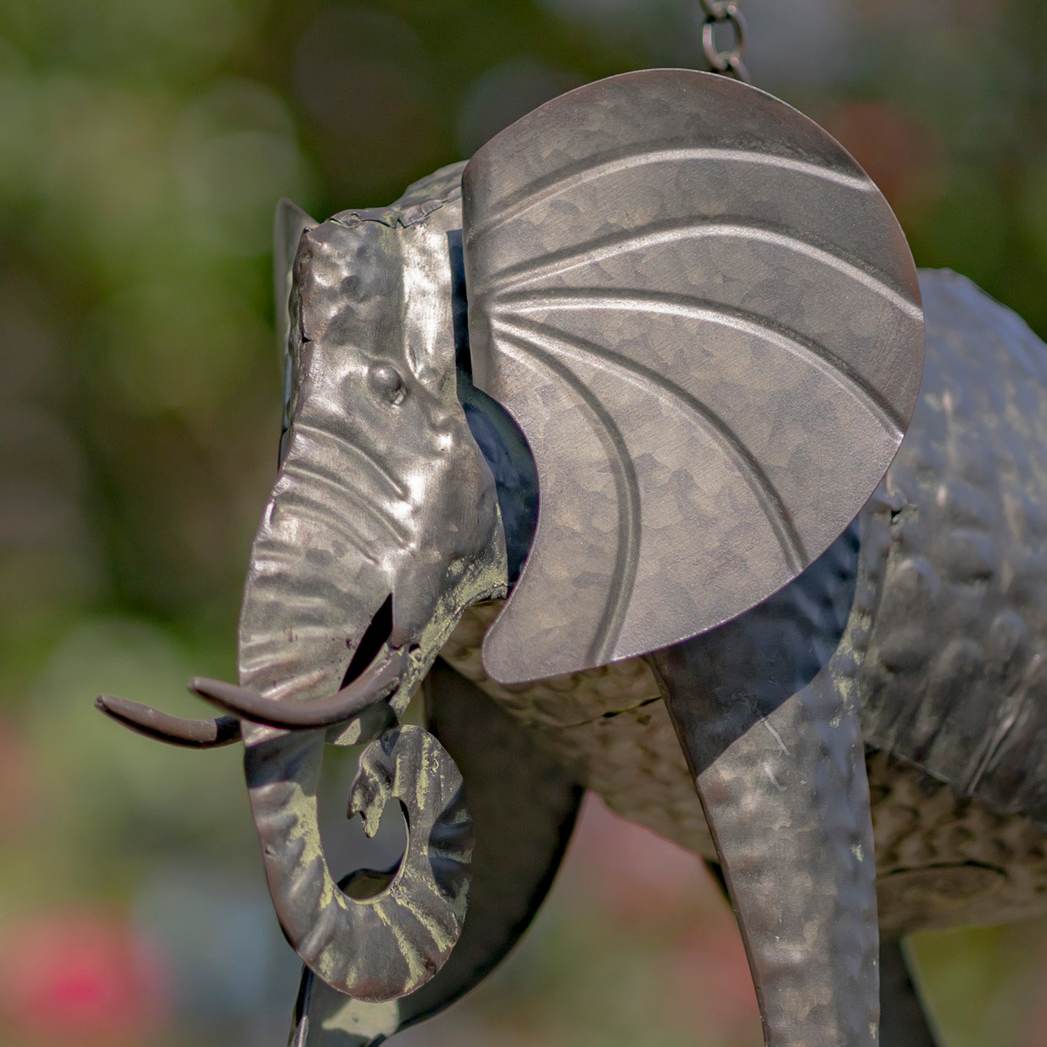 Metallic elephant sculpture with detailed design against a blurred natural background