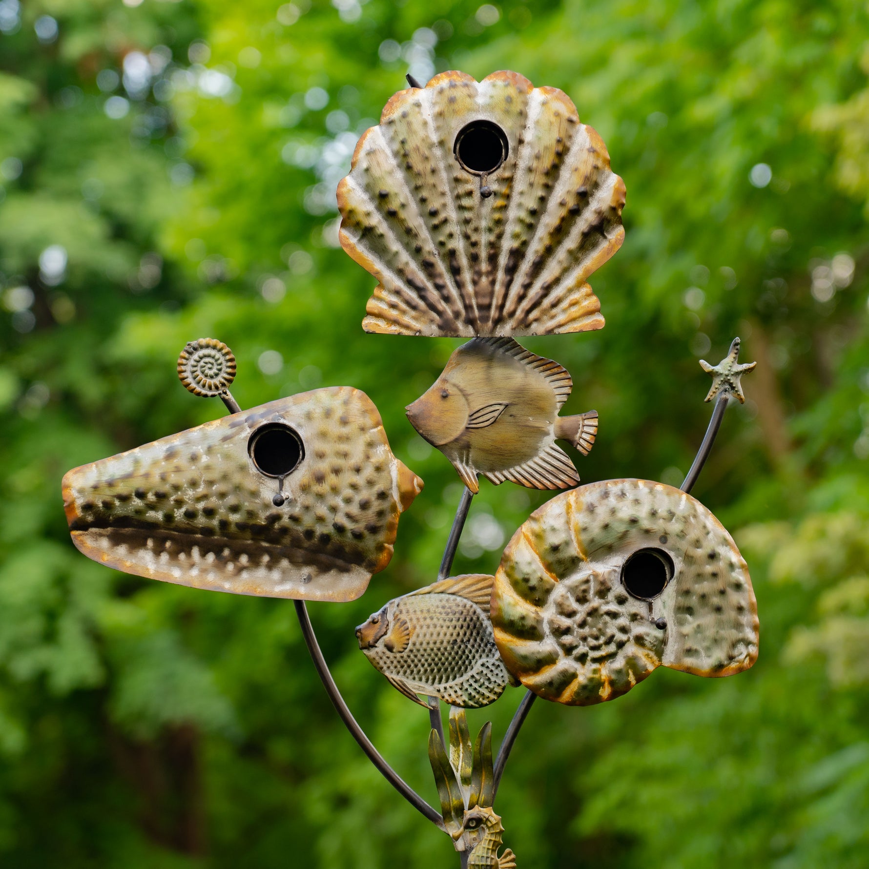 Decorative metal sculpture of seashells with fish on a green leafy background