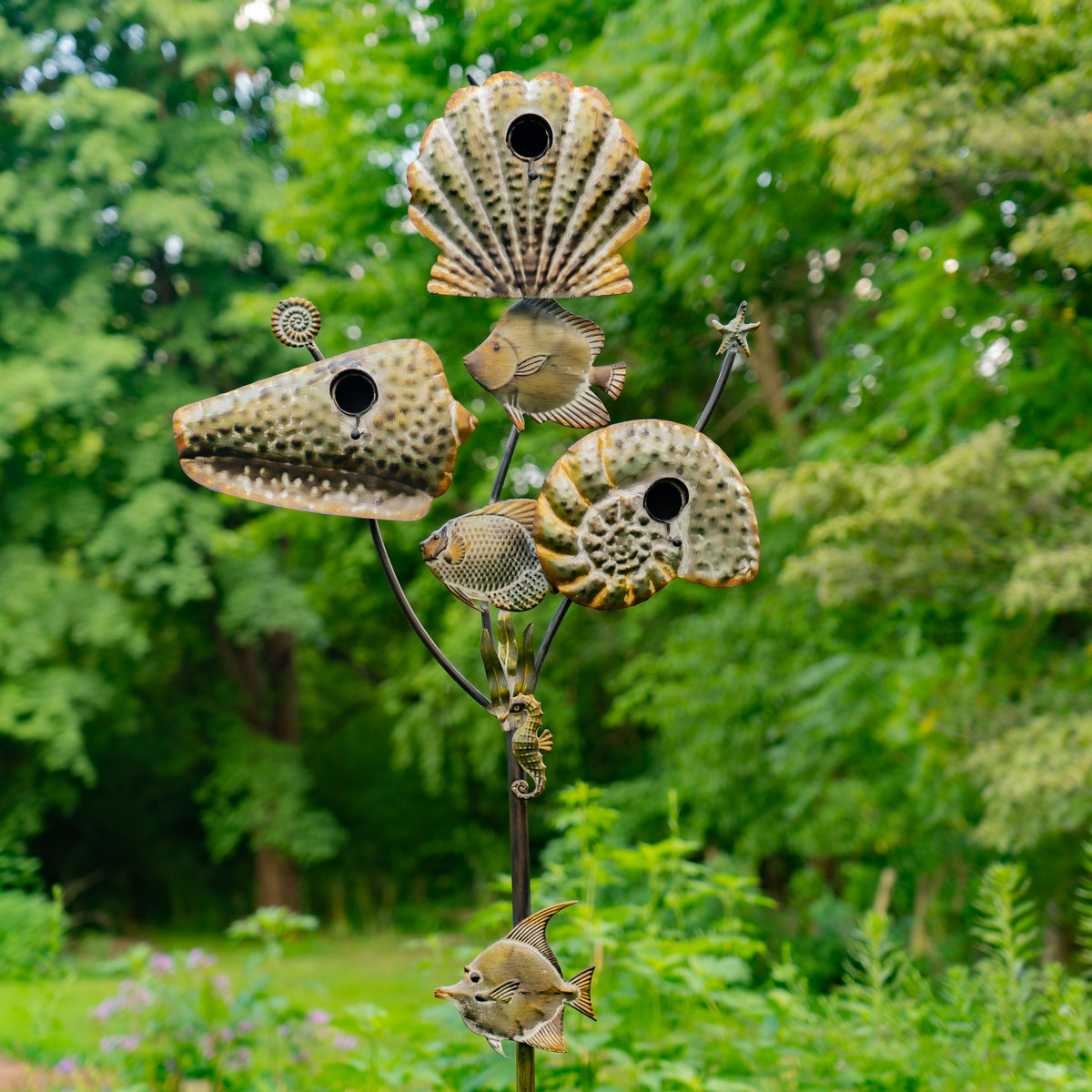 Metallic fish and shell-shaped birdhouses on a stand with a natural green background