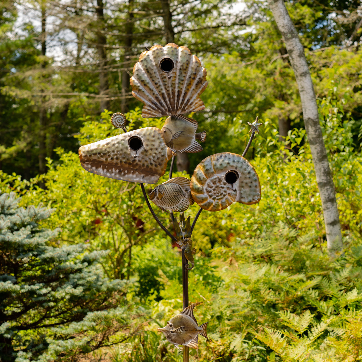 Decorative metal sculpture resembling a fish with multiple heads in a forest setting