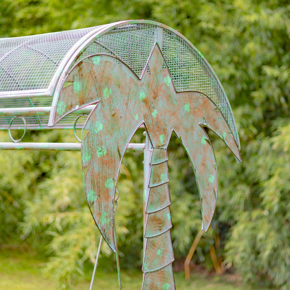 Decorative metal palm tree sculpture with a greenish patina against a blurred natural background