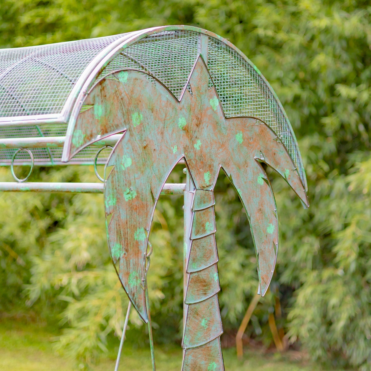 Decorative metal palm tree sculpture with a greenish patina against a blurred natural background