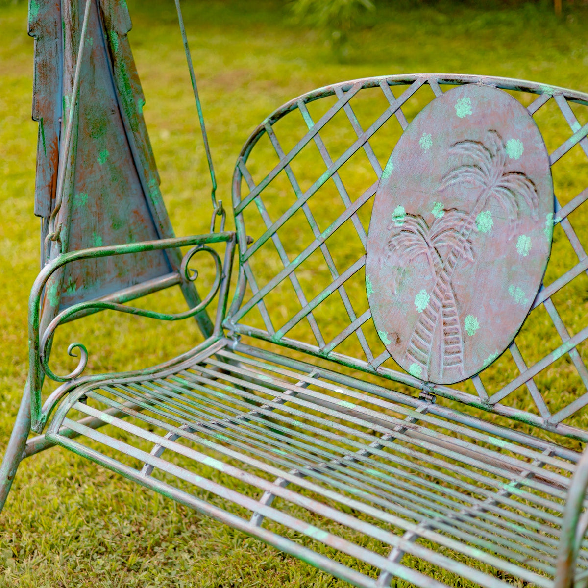 Worn metal garden bench with decorative backrest on a grassy background