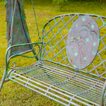 Worn metal garden bench with decorative backrest on a grassy background