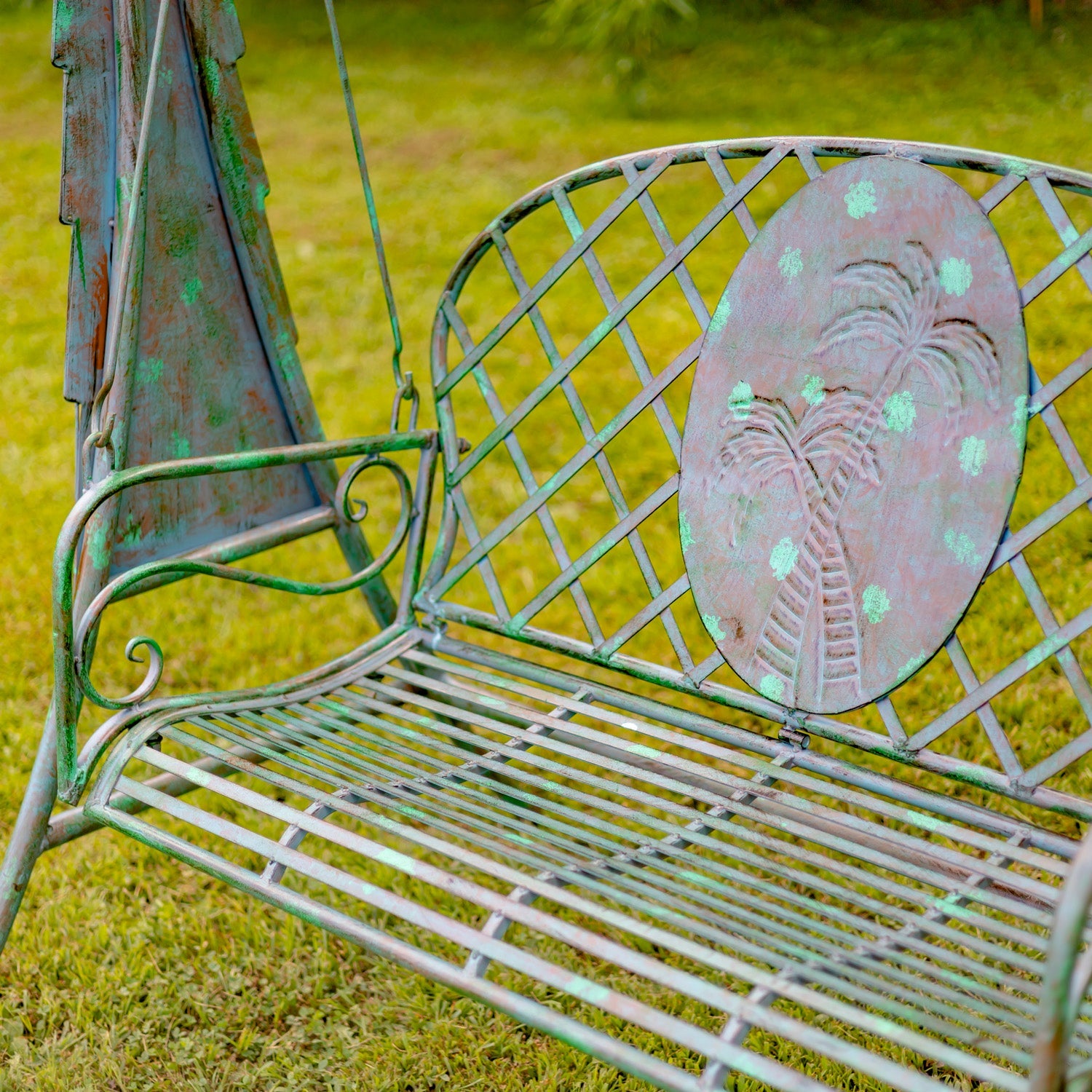 Worn metal garden bench with decorative backrest on a grassy background