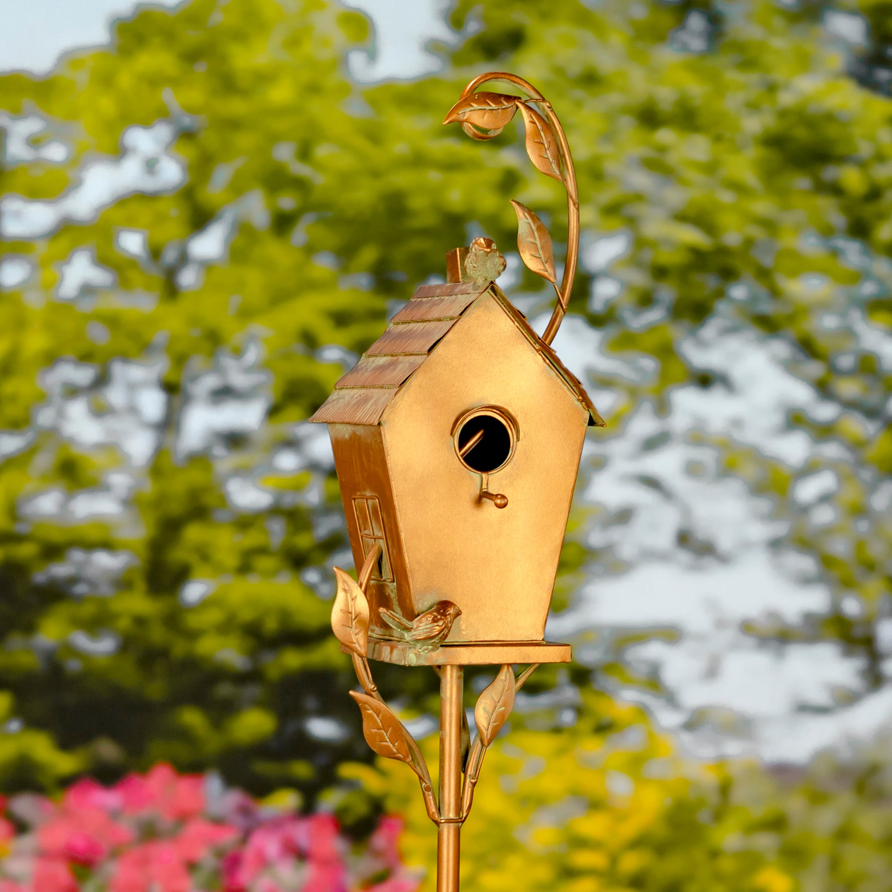 Decorative gold birdhouse with leaf design on a stand against a blurred natural background