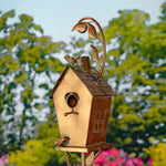 Decorative birdhouse with a metal leaf on top against a blurred garden background