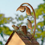 Decorative metal birdhouse with a bird perched on top, against a blurred natural background.