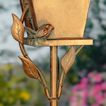 Bronze bird feeder with a bird perched on it, against a blurred garden background.