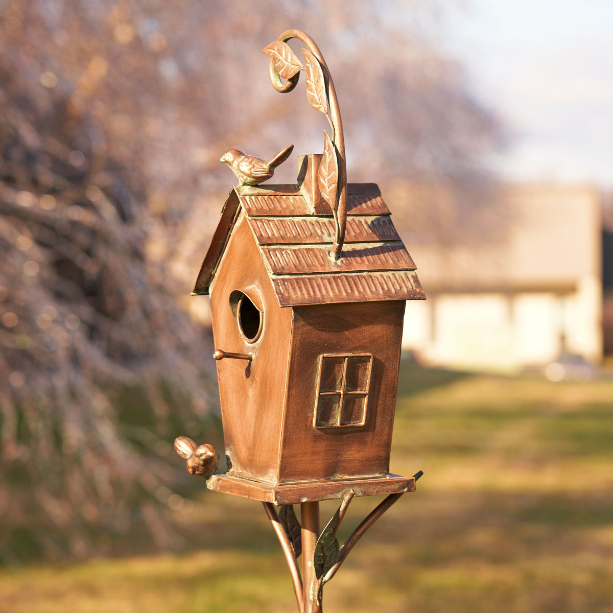 Bronze birdhouse with decorative elements on a blurred outdoor background