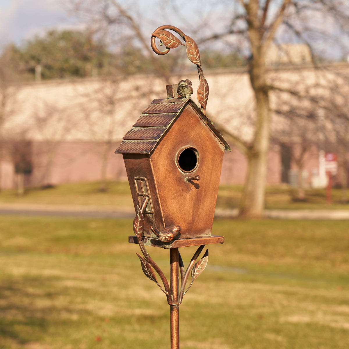 Decorative copper birdhouse on a stand in a park setting