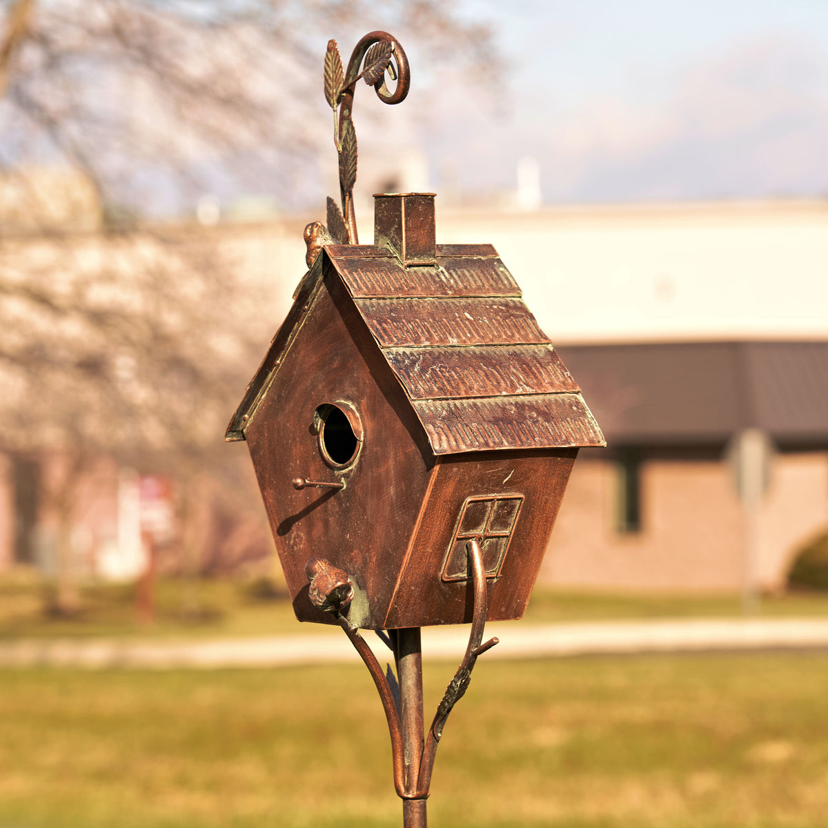 Bronze birdhouse on a stand with a blurred background