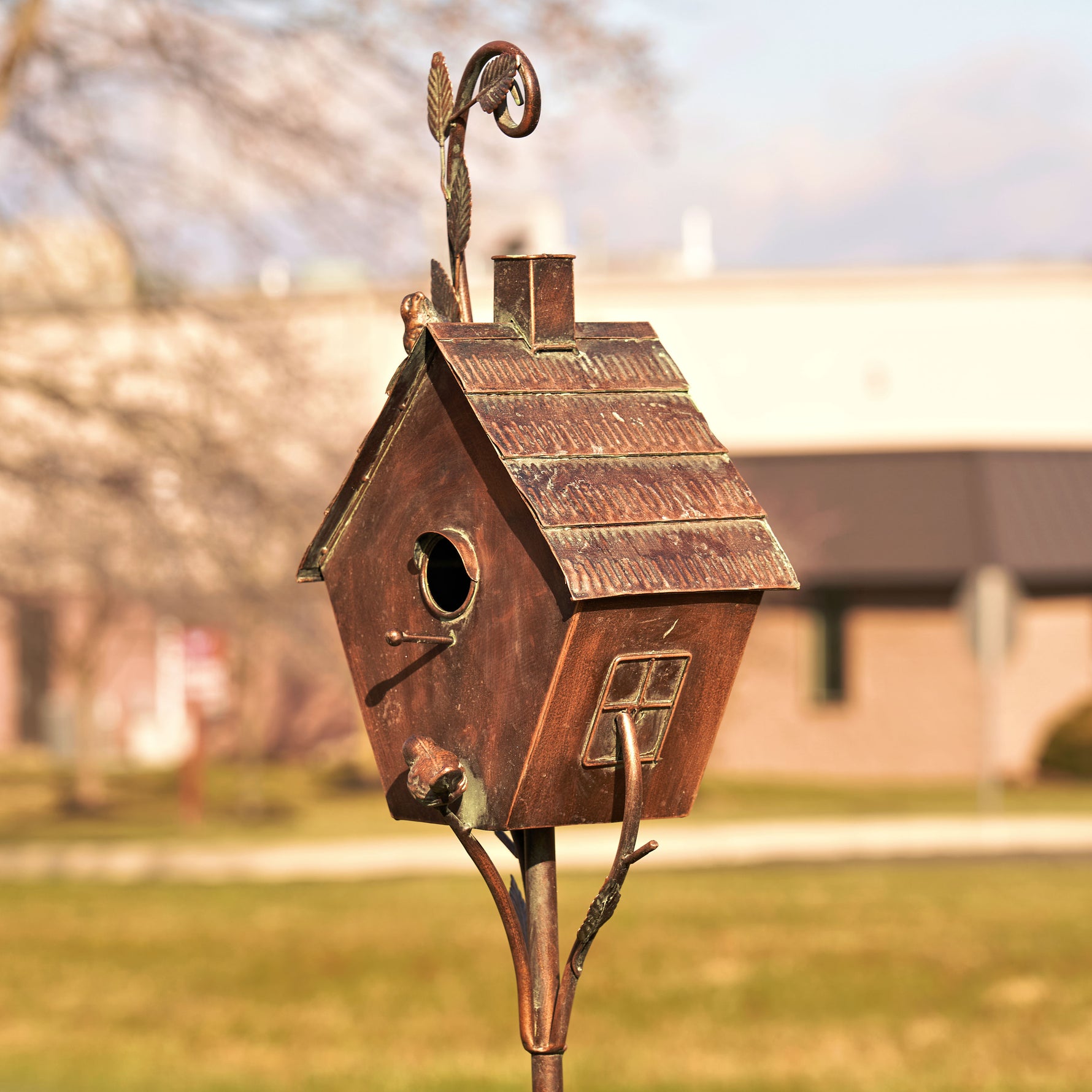 Bronze birdhouse on a stand with a blurred background