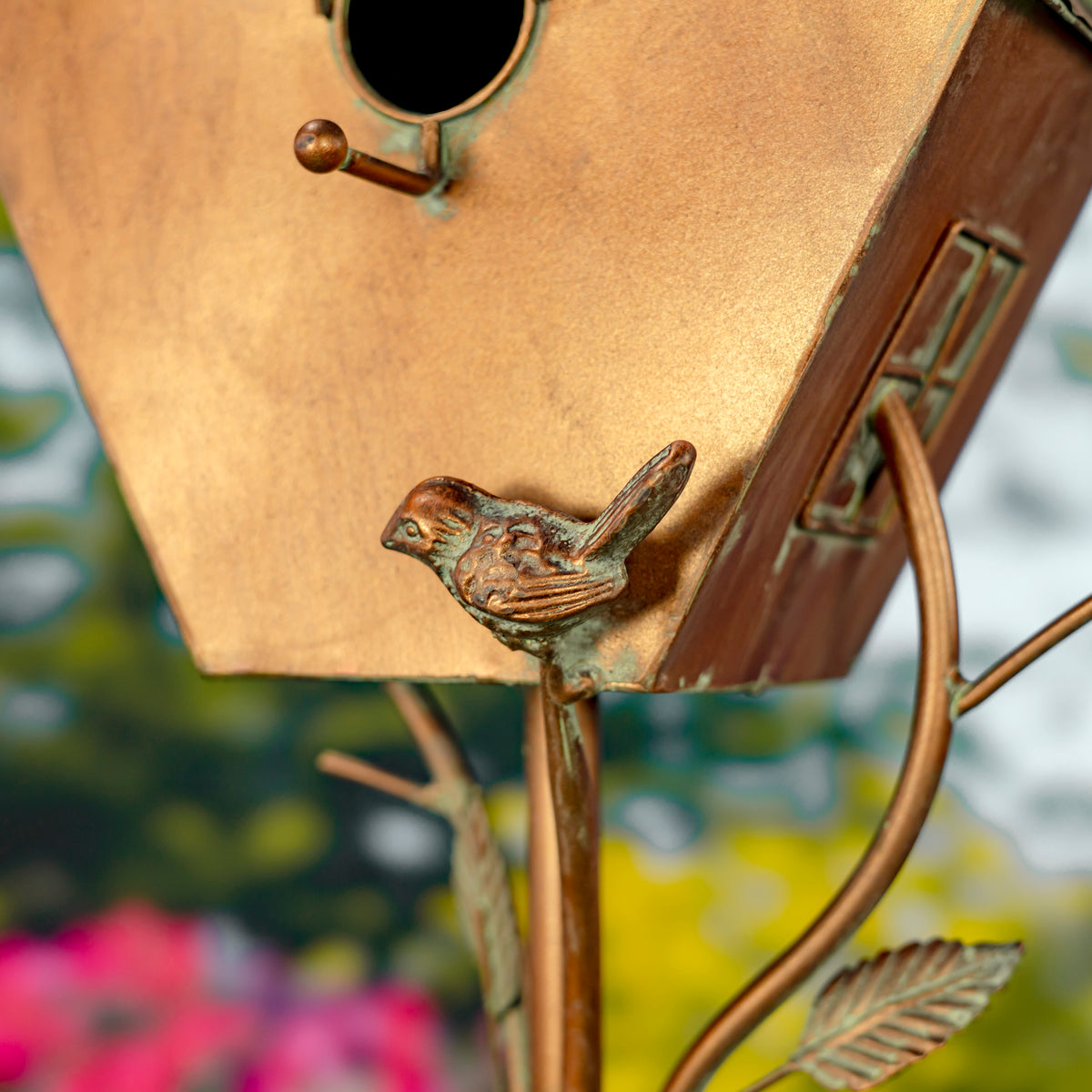 Bronze birdhouse with a bird ornament against a blurred garden background