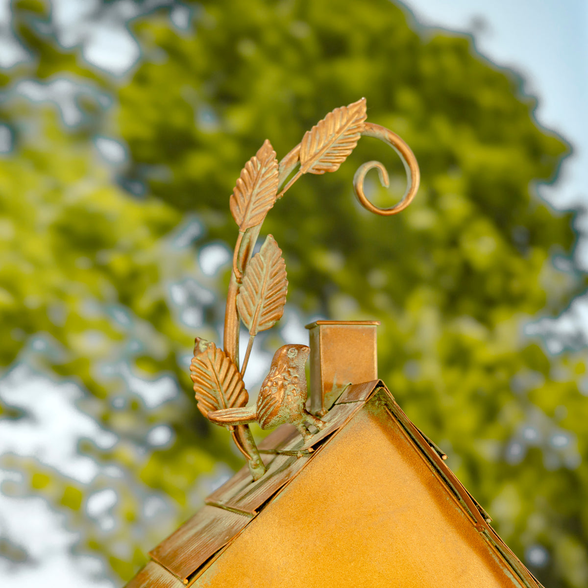 Decorative metal birdhouse with leaf and vine design against a blurred green background